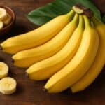 Un casco di banane con alcune fette accanto su tavolo in legno con foglie tropicali