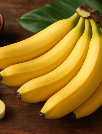 Un casco di banane con alcune fette accanto su tavolo in legno con foglie tropicali