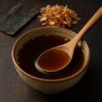 Ciotola di ceramica con brodo dashi, cucchiaio in legno, kombu e katsuobushi sullo sfondo