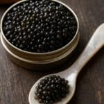 Caviale nero in una scatoletta metallica con cucchiaio in madreperla su fondo rustico