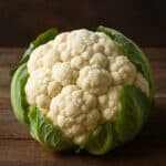 Cavolfiore intero su fondo rustico con foglie verdi fresche e testa bianca compatta