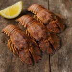 Tre cicale di mare (Scyllarides latus) disposte su tavolo di legno con spicchio di limone