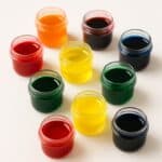 Barattolini trasparenti con coloranti alimentari liquidi di vari colori su sfondo bianco
