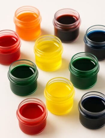 Barattolini trasparenti con coloranti alimentari liquidi di vari colori su sfondo bianco