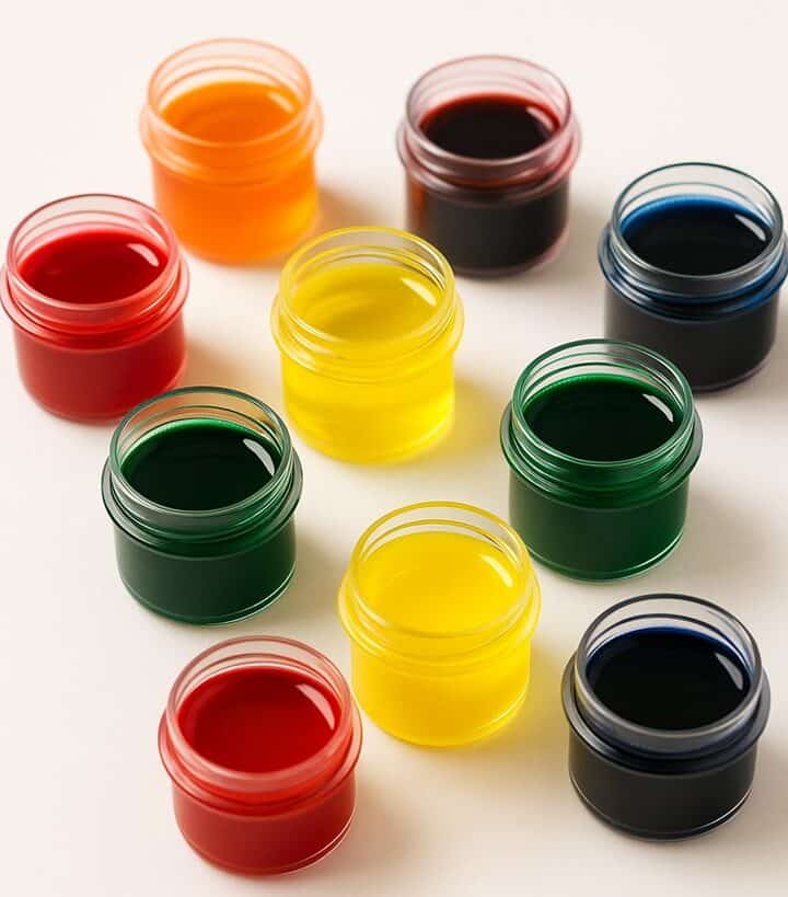 Barattolini trasparenti con coloranti alimentari liquidi di vari colori su sfondo bianco