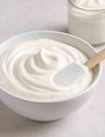 Crema Alba bianca e lucida in ciotola con spatola in silicone su sfondo chiaro