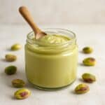Barattolo di crema di pistacchi con cucchiaio in legno e pistacchi sgusciati attorno