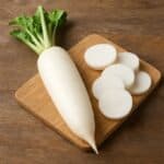 Daikon fresco intero con foglie verdi e fette affettate su tagliere