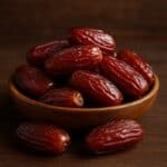 Datteri lucidi e rugosi in ciotola di legno con alcuni frutti sparsi sul tavolo