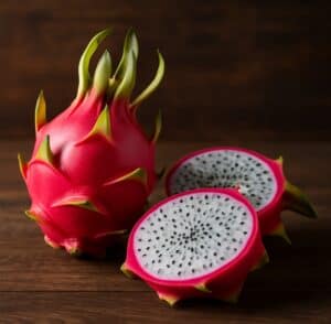 Dragon fruit Pitaya intera e due metà tagliate con polpa bianca e semi neri su fondo rustico