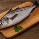 Eglefino intero crudo su tagliere di legno con prezzemolo