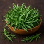 Erba Stella (Plantago coronopus) con foglie verdi a forma di stella in ciotola di legno su tavolo scuro