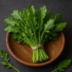 Mazzo di erbette di campo fresche con foglie verdi frastagliate in ciotola di legno su fondo scuro