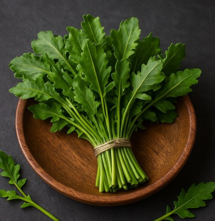 Mazzo di erbette di campo fresche con foglie verdi frastagliate in ciotola di legno su fondo scuro