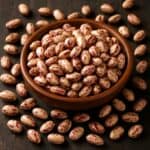 Fagioli borlotti crudi in ciotola di legno con chicchi sparsi su tavolo scuro