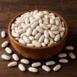 Fagioli cannellini secchi in ciotola rustica con chicchi sparsi su legno scuro
