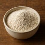 Ciotola piena di farina di avena chiara e leggermente granulosa su fondo in legno