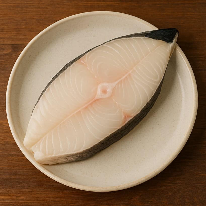 Trancio di halibut fresco con pelle scura e carne chiara disposto su piatto chiaro