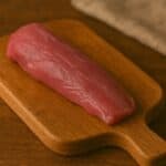 Filetto di agnello rosa intenso su tagliere con manico in legno caldo