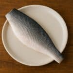 Filetto di branzino con pelle grigia e carne chiara su piatto tondo