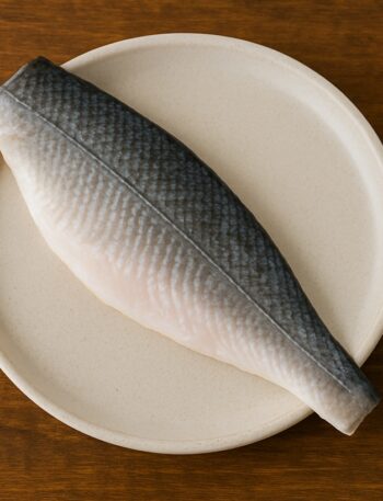 Filetto di branzino con pelle grigia e carne chiara su piatto tondo