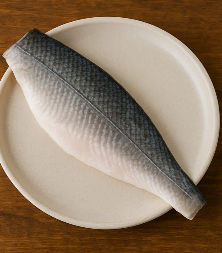 Filetto di branzino con pelle grigia e carne chiara su piatto tondo