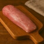 Filetto di maiale rosa chiaro su tagliere in legno con sfondo rustico