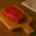 Medaglione di filetto di manzo rosso vivo su tagliere in legno rustico