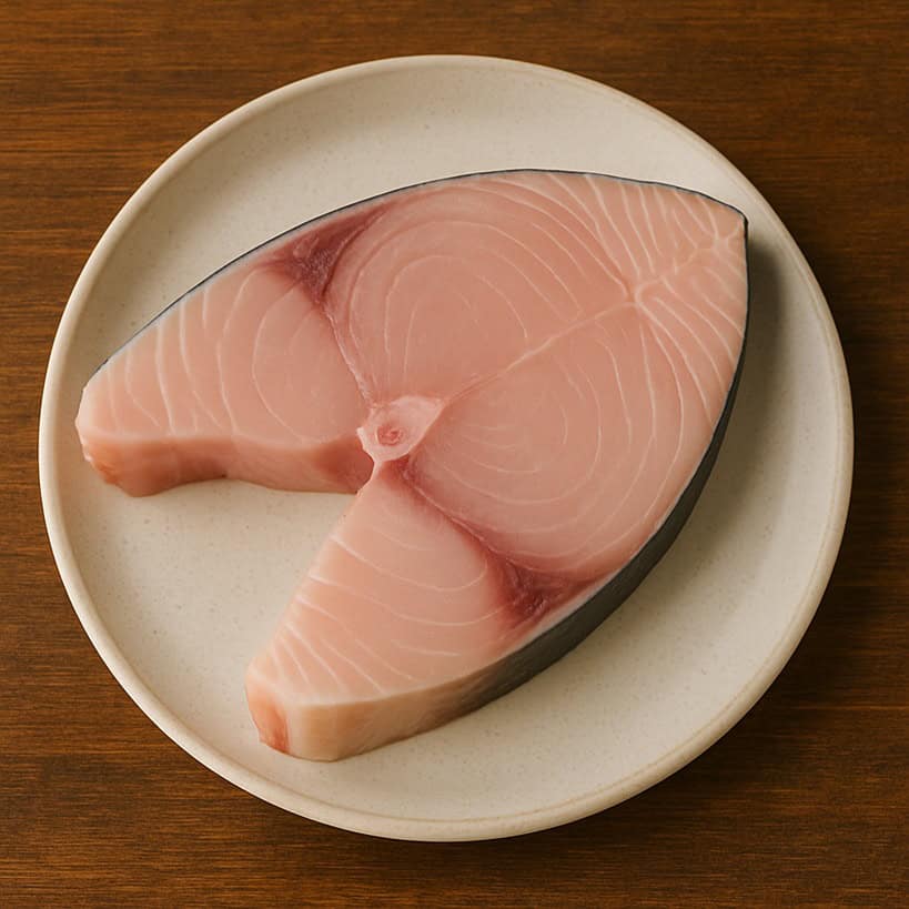 Trancio di pesce spada crudo con carne rosa chiaro e bordo scuro su piatto chiaro