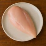 Petto di pollo crudo senza pelle né osso su piatto tondo chiaro
