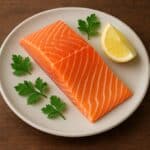 Trancio di salmone crudo su piatto chiaro con spicchio di limone e foglie di prezzemolo