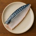 Trancio di sgombro con pelle argentata e striature nere su piatto in ceramica