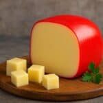 Formaggio Edam intero con cera rossa e cubetti su tagliere in legno