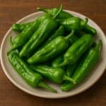 Peperoncini friggitelli verdi crudi disposti su piatto chiaro sopra tavolo rustico