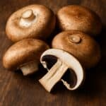 Quattro funghi Portobello freschi, uno dei quali tagliato a metà, su sfondo in legno