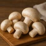 Funghi champignon bianchi su tagliere di legno con sfondo rustico sfocato
