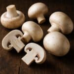 Funghi prataioli bianchi interi e a metà disposti su tavolo in legno scuro