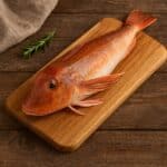 Gallinella di mare intera cruda su tagliere di legno con rametto di rosmarino