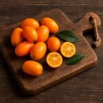 Kumquat interi e tagliati appoggiati su un tagliere in legno naturale