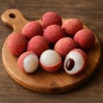 Litchi interi e aperti che mostrano la polpa bianca e il seme su tagliere rotondo di legno naturale