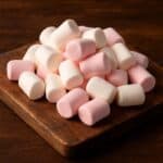 Marshmallows cilindrici bianchi e rosa su tagliere rustico in legno scuro