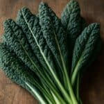 Foglie di cavolo nero intere e arricciate disposte su un piano in legno grezzo