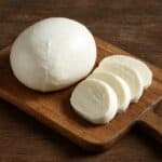 Mozzarella intera e a fette su tagliere di legno rustico