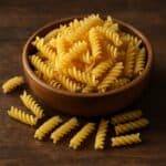 Formato di pasta eliche, in ciotola di legno con pasta sparsa su tavolo in legno