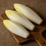 Indivia belga fresca disposta su tagliere in legno con sfondo in juta naturale