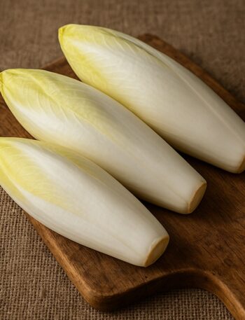 Indivia belga fresca disposta su tagliere in legno con sfondo in juta naturale