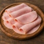 Fette sottili di prosciutto cotto arrotolate su tagliere in legno