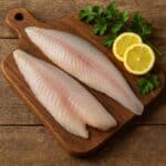 Filetti di pesce persico su tagliere in legno con limone ed erbe