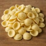 Un primo piano di orecchiette fresche disposte su un tagliere rustico di legno, pronte per essere cucinate.