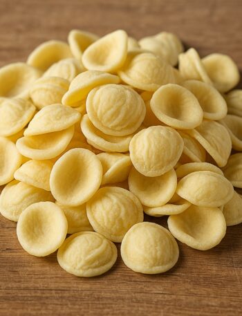 Un primo piano di orecchiette fresche disposte su un tagliere rustico di legno, pronte per essere cucinate.